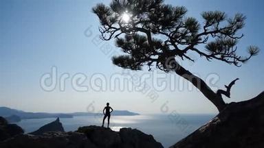 瘦削，运动的旅游女孩<strong>站在山顶</strong>上，在悬崖下欣赏令人叹为观止的海景和非常明亮的太阳